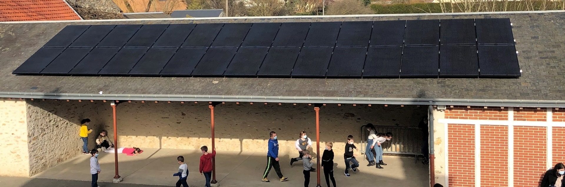 Un préau d'école avec des panneaux solaires sur le toit et des enfants qui s'amusent dans la cour